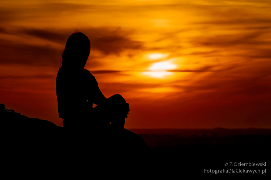 Postać kobieca na tle zachodzącego słońca i podświetlonego nieba